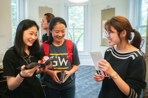 Three students, one wearing a GW t-shirt, smiling and talking in a group